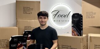 Emre Tuncer hält eine schwarze Springform, um ihn stehen Versandkartons und verpackte Backformen von Food with Style vor dem beleuchteten Firmenschild