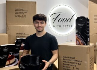 Food with Style: Vom Backvideo mit der Mutter zur eigenen Backform-Marke Emre Tuncer hält eine schwarze Springform, um ihn stehen Versandkartons und verpackte Backformen von Food with Style vor dem beleuchteten Firmenschild