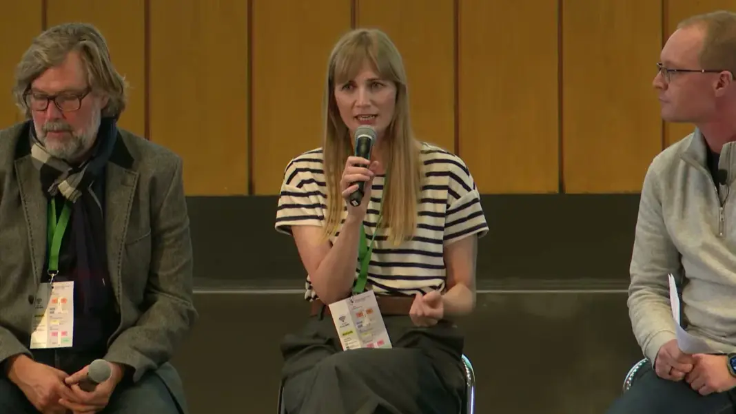 Teilnehmende des Panels Funding the Future auf der Bühne des Audimax, eine Frau im gestreiften Shirt spricht ins Mikrofon