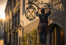 Handwerksmeister montiert ein schmiedeeisernes Zunftschild über dem Eingang seiner neuen Werkstatt