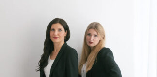 Die Gruenderinnen Carolin Krebber und Leonie Dowling stehen in dunklen Anzuegen nebeneinander vor einer hellen Wand