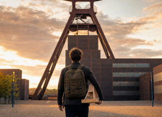 Gründer mit Rucksack vor dem Förderturm der Zeche Zollverein im Abendlicht