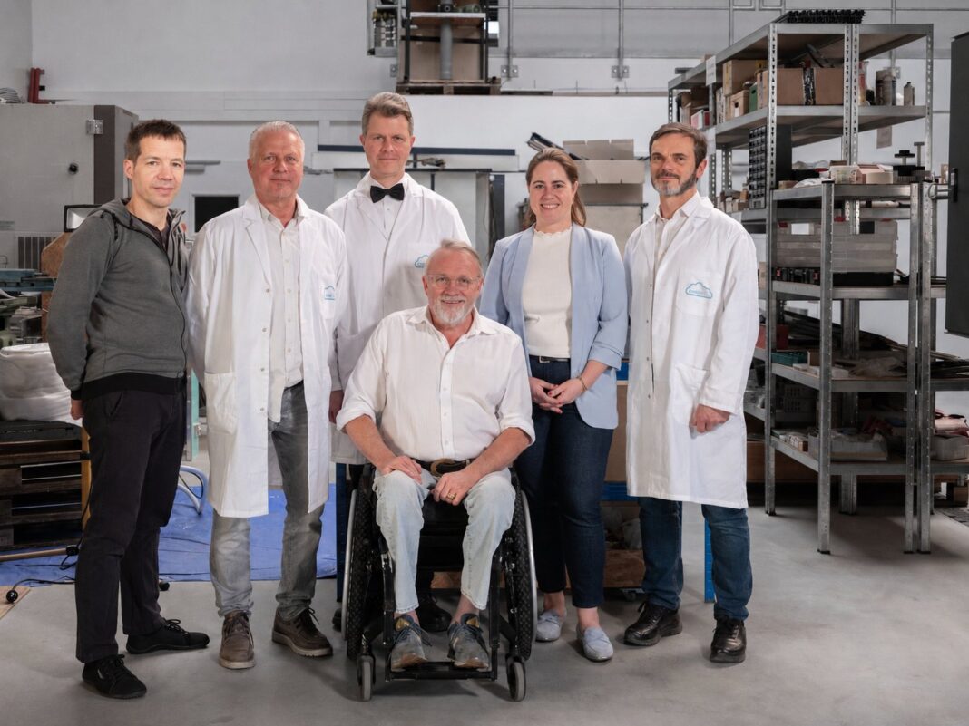 Das Team von HEIONTEC steht in einer Werkhalle, einer der Gründer sitzt im Rollstuhl