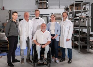 Das Team von HEIONTEC steht in einer Werkhalle, einer der Gründer sitzt im Rollstuhl
