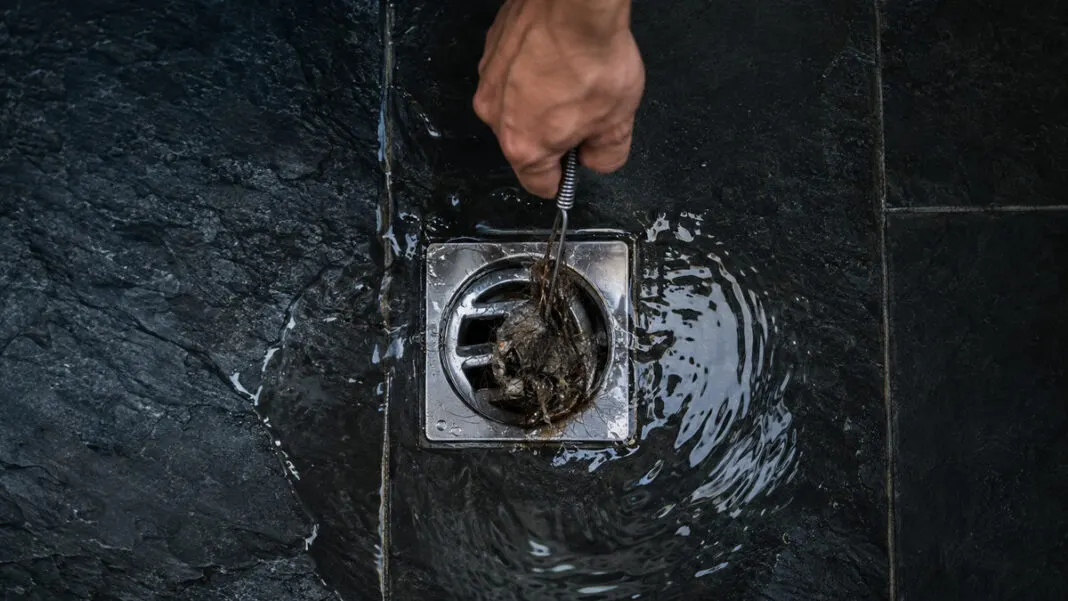 Stehendes Wasser rund um einen verstopften Duschabfluss auf dunklen Schieferfliesen