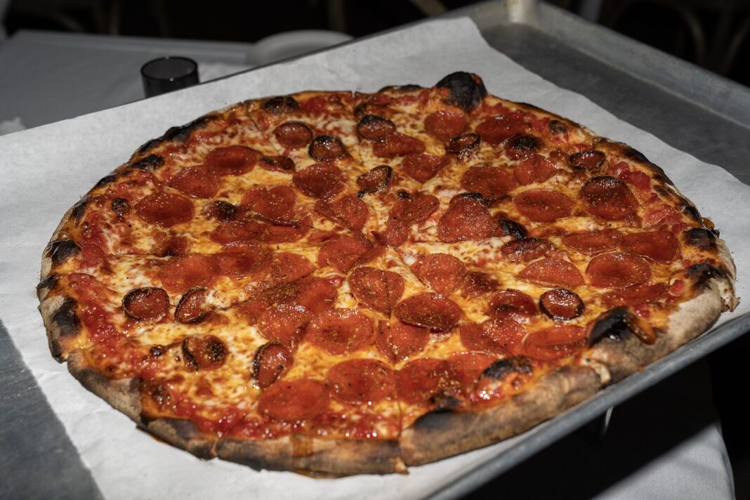 Pizzastueck mit Salami, auf das goldener Hot Honey getraeufelt ist