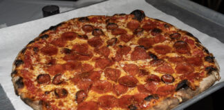 Pizzastueck mit Salami, auf das goldener Hot Honey getraeufelt ist