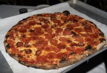 Pizzastueck mit Salami, auf das goldener Hot Honey getraeufelt ist