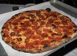 Pizzastueck mit Salami, auf das goldener Hot Honey getraeufelt ist