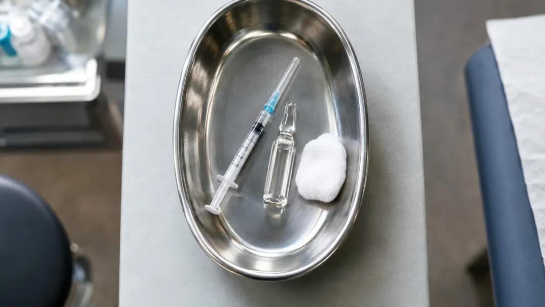 Einwegspritze und Ampulle mit klarer Lösung in einer Nierenschale aus Edelstahl neben einem Tupfer