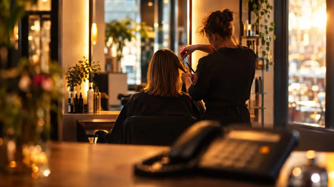 Friseurin schneidet einer Kundin die Haare, im Vordergrund ein Telefon auf dem Empfangstresen