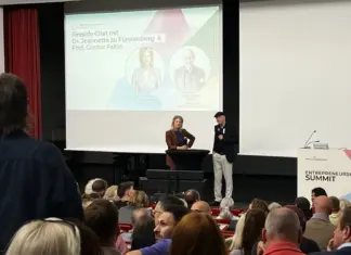 Jeannette zu Fürstenberg und Günter Faltin auf der Bühne des Entrepreneurship Summit 2026 vor der Leinwand mit der Ankündigung ihres Fireside Chats, davor das Publikum
