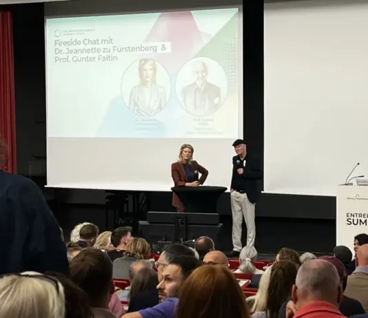 Jeannette zu Fürstenberg und Günter Faltin auf der Bühne des Entrepreneurship Summit 2026 vor der Leinwand mit der Ankündigung ihres Fireside Chats, davor das Publikum