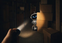 Taschenlampe entdeckt einen kleinen Roboter hinter Kartons im Lager