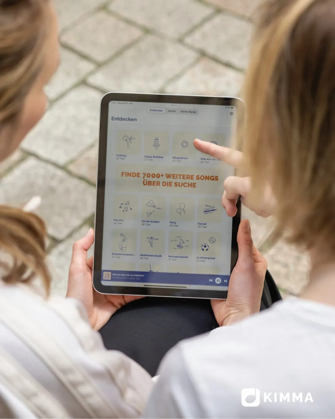 Zwei Frauen wählen auf einem Tablet Musik in der KIMMA-App aus