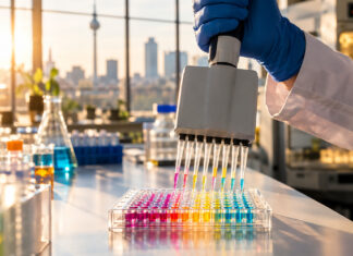 Sondermodell LifeScience-Gründungen – Wie sie gelingen und warum diese anders als übliche Gründungen sind Mehrkanalpipette über einer Mikrotiterplatte im Labor eines Berliner Biotech-Startups, im Hintergrund der Fernsehturm