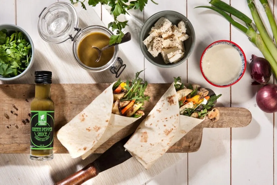 Zwei Wraps mit Gemüse auf einem Holzbrett, daneben eine Flasche Green Pepper Sauce von Mexican Tears