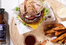 Mexican Tears bei der Höhle der Löwen: Wiedersehen nach zwölf Jahren Burger mit Pommes auf einem Holzbrett, daneben eine Flasche Carolina Reaper Sauce von Mexican Tears und ein Schälchen Sauce