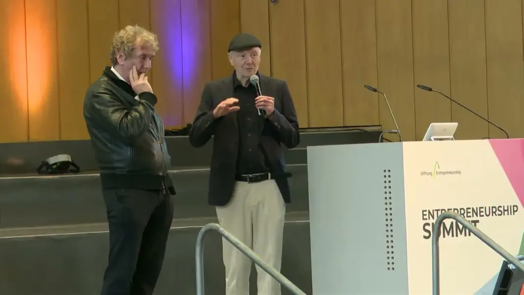 Michael Braungart in Lederjacke und Günter Faltin mit Mikrofon stehen neben dem Rednerpult mit dem Schriftzug Entrepreneurship Summit