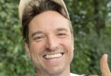 Laurens Laudowicz mit heller Kappe lacht vor grünem Laub und zeigt den Daumen nach oben