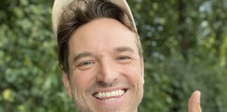 Laurens Laudowicz mit heller Kappe lacht vor grünem Laub und zeigt den Daumen nach oben