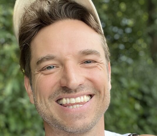Laurens Laudowicz mit heller Kappe lacht vor grünem Laub und zeigt den Daumen nach oben