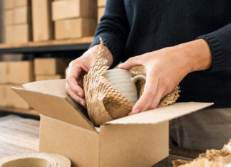 Hände verpacken eine Tasse in Graspapier und recycelte Pappe