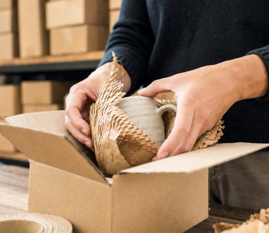 Hände verpacken eine Tasse in Graspapier und recycelte Pappe