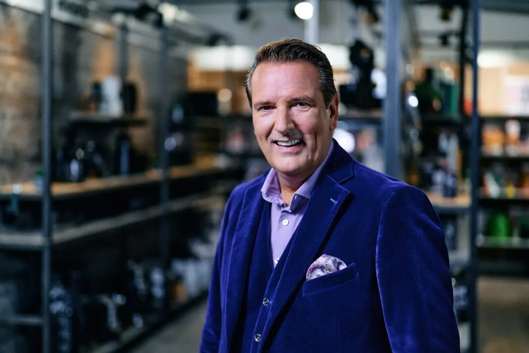 Ralf Duemmel im blauen Samtanzug laechelt im Showroom von DS Produkte