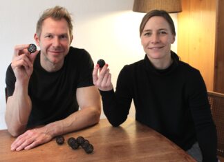Susanne und Bernd Schmekel, die Erfinder der Sauberkugel, halten an einem Holztisch je eine Sauberkugel in die Kamera