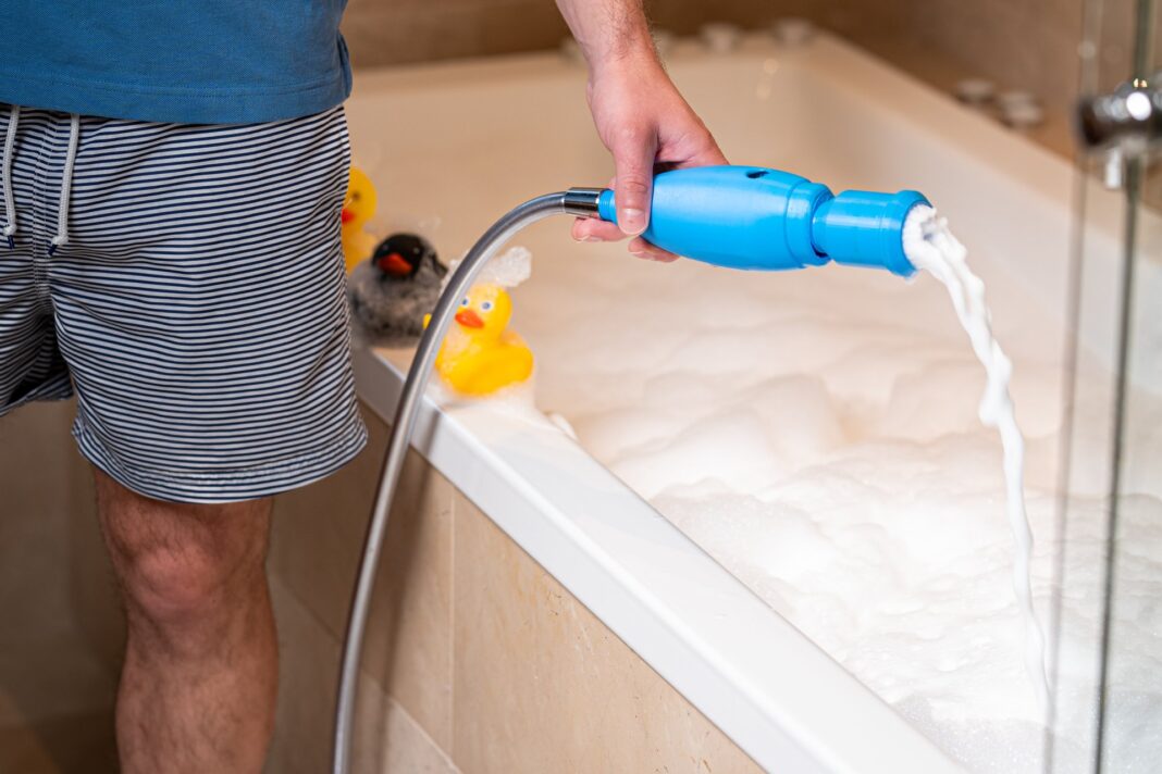 SchaumPo nach der Höhle der Löwen Ein Mann füllt mit dem blauen SchaumPo-Gerät am Duschschlauch Schaum in eine Badewanne, auf dem Wannenrand sitzen Quietscheenten