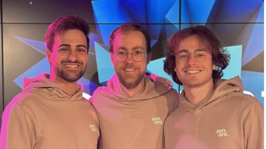 Die drei Senani-Gründer in beigen Senani-Hoodies lächeln vor einer blau beleuchteten Wand beim Road to Summit 2025 in Stuttgart