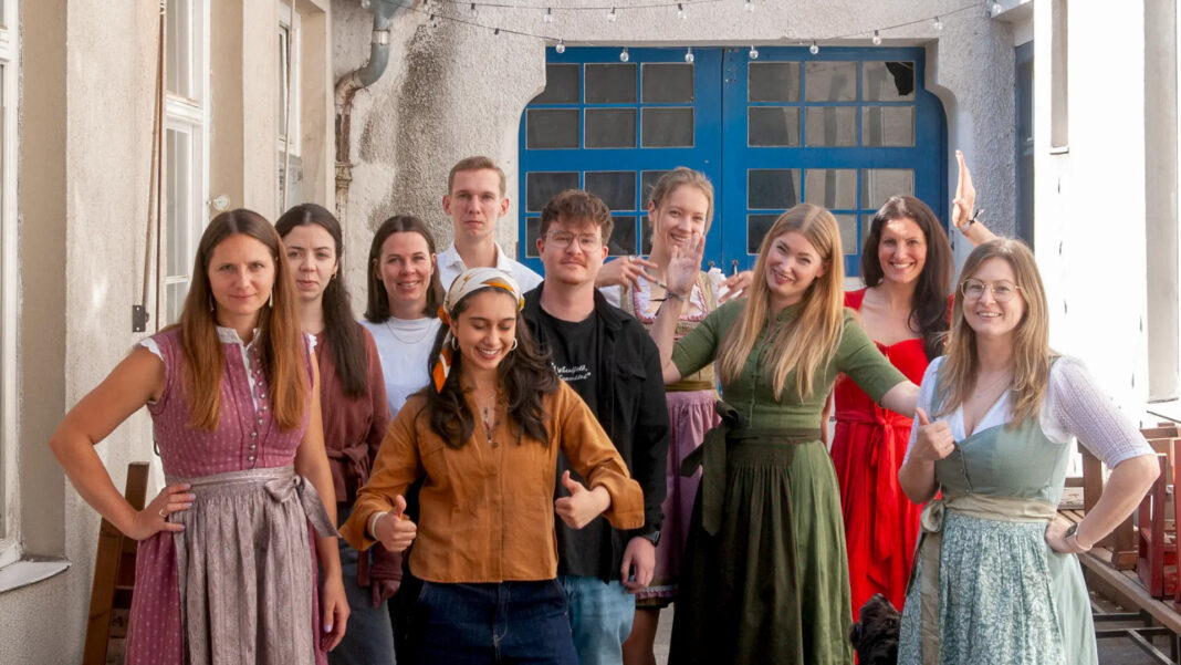 Das Team von meinhaus.digital steht in Tracht auf einem Innenhof vor einer blauen Holztuer