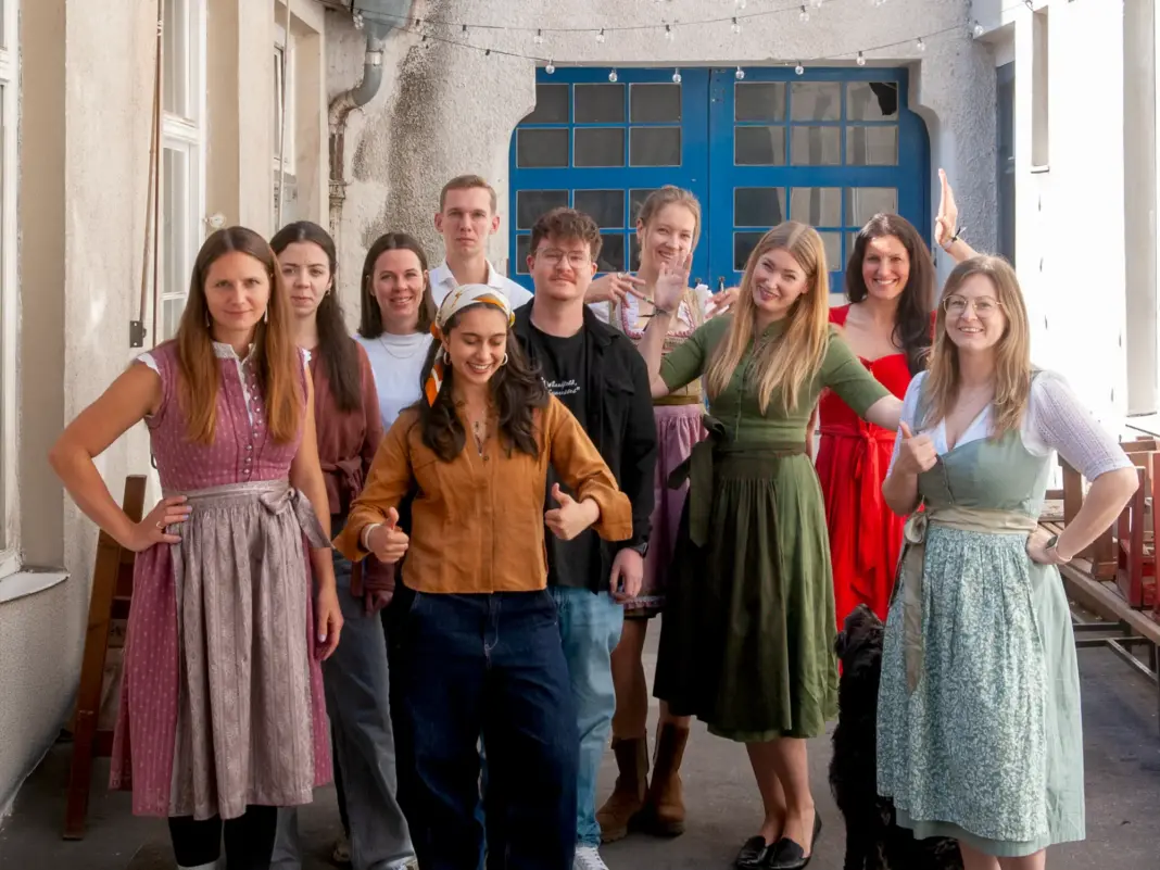 Das Team von meinhaus.digital steht in Tracht auf einem Innenhof vor einer blauen Holztuer