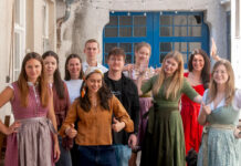 Das Team von meinhaus.digital steht in Tracht auf einem Innenhof vor einer blauen Holztuer