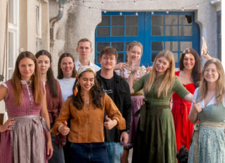 Das Team von meinhaus.digital steht in Tracht auf einem Innenhof vor einer blauen Holztuer