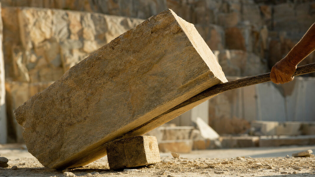 Mit einer langen Eisenstange wird ein großer Steinblock angehoben Mit einer langen Eisenstange wird ein großer Steinblock angehoben