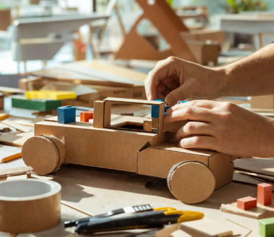 Hände bauen aus Pappe und bunten Holzklötzen einen ersten Prototyp