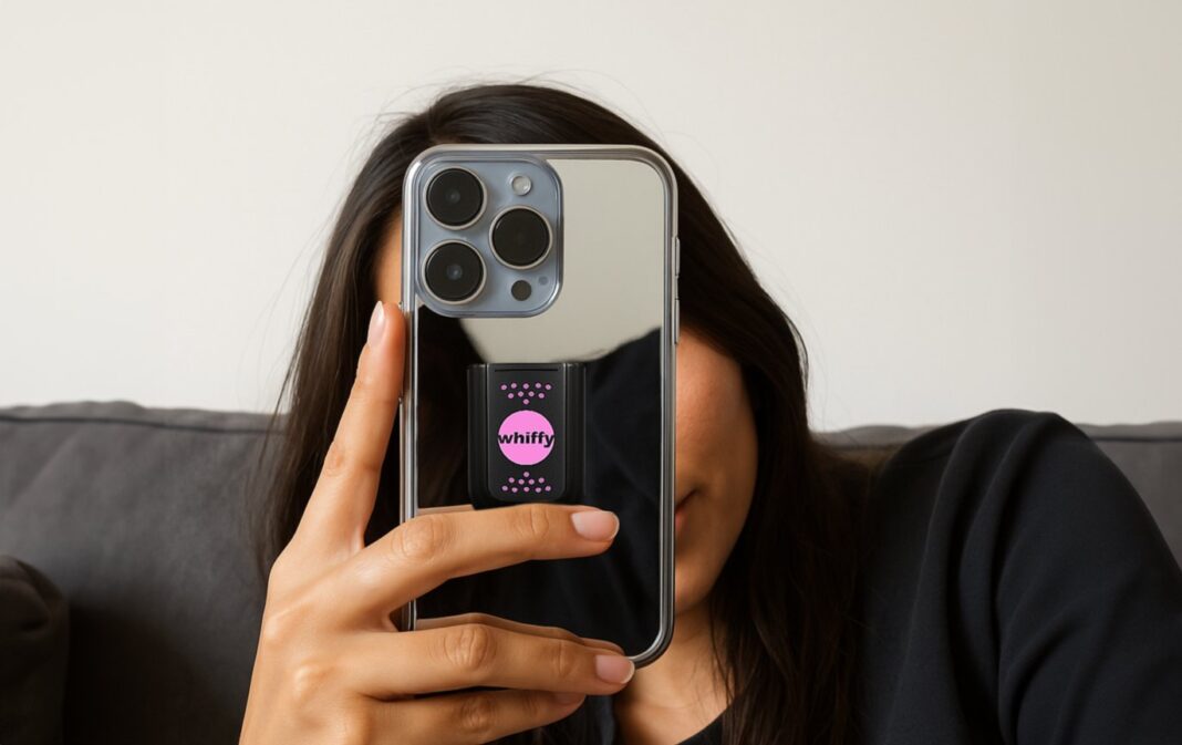 Eine Frau hält ein Smartphone vors Gesicht, auf dessen Rückseite eine whiffy-Halterung mit rosa Kapsel klebt