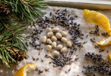 Kleine runde Kapseln liegen zwischen getrockneten Lavendelblüten, Zirbelkiefernzweigen und Zitronenschalen auf einem Leinentuch