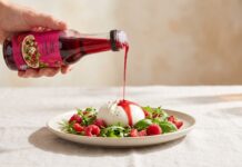 Himbeer-Dressing von Wunderdressing wird aus der Flasche über Burrata mit Himbeeren und Rucola gegossen