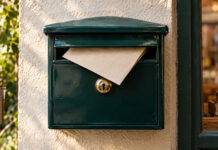 Zahlungserinnerung schreiben: Formulierung, Frist und Muster Ein cremefarbener Leinenumschlag steckt zur Hälfte in der Klappe eines emaillierten Wandbriefkastens, das Messingschloss blank gegriffen, weiches Morgenlicht von der Seite
